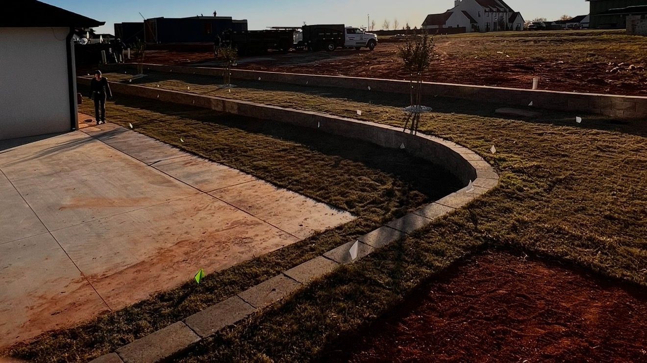 Curved concrete walkway beside a grassy dirt lot and houses under construction at sunset