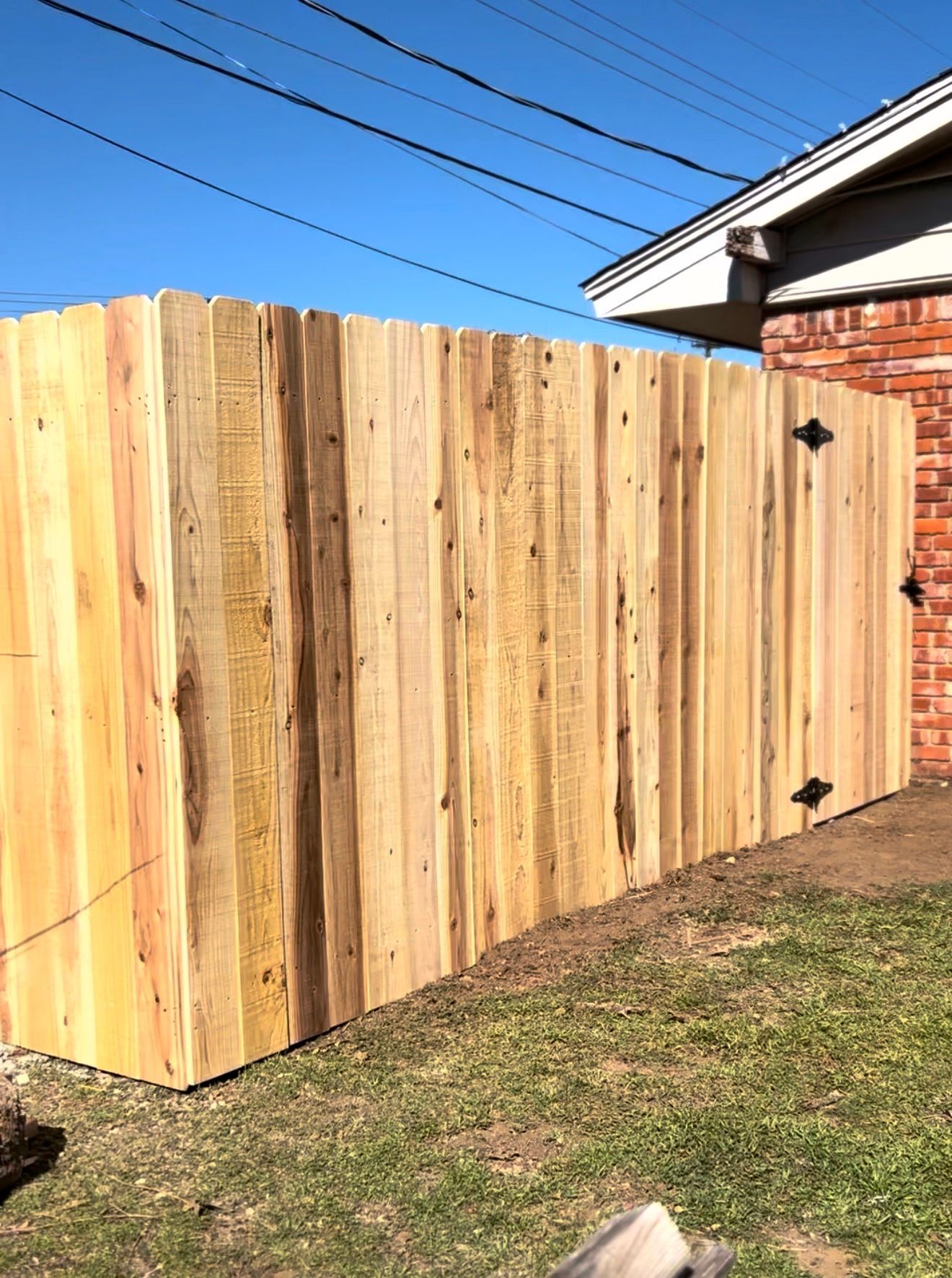 New wooden fence beside a house on a sunny day, with grass and blue sky visible