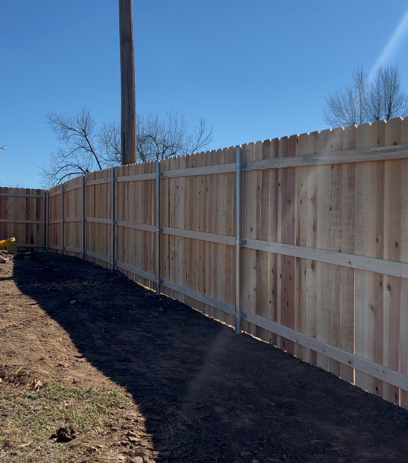 Wooden privacy fence along a black mulch path under a clear blue sky