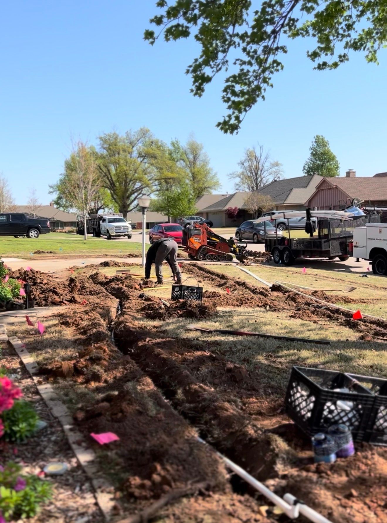 Workers trenching a yard beside houses and parked vehicles on a sunny day