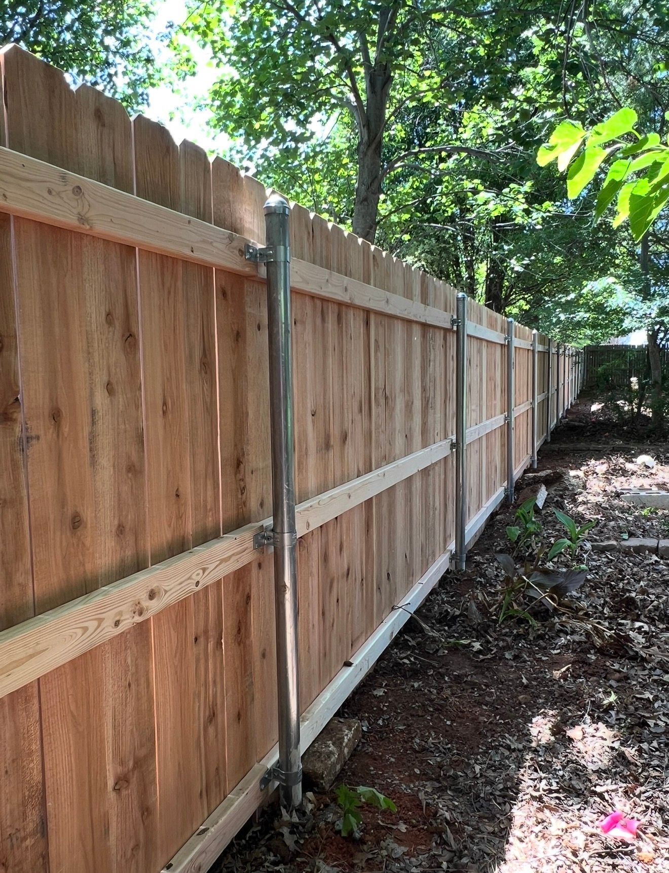 Wooden privacy fence with metal posts along a leafy backyard boundary