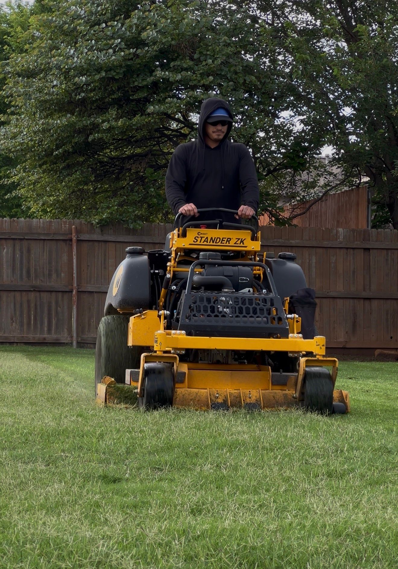 Person mowing grass on a yellow riding lawn mower in a backyard.