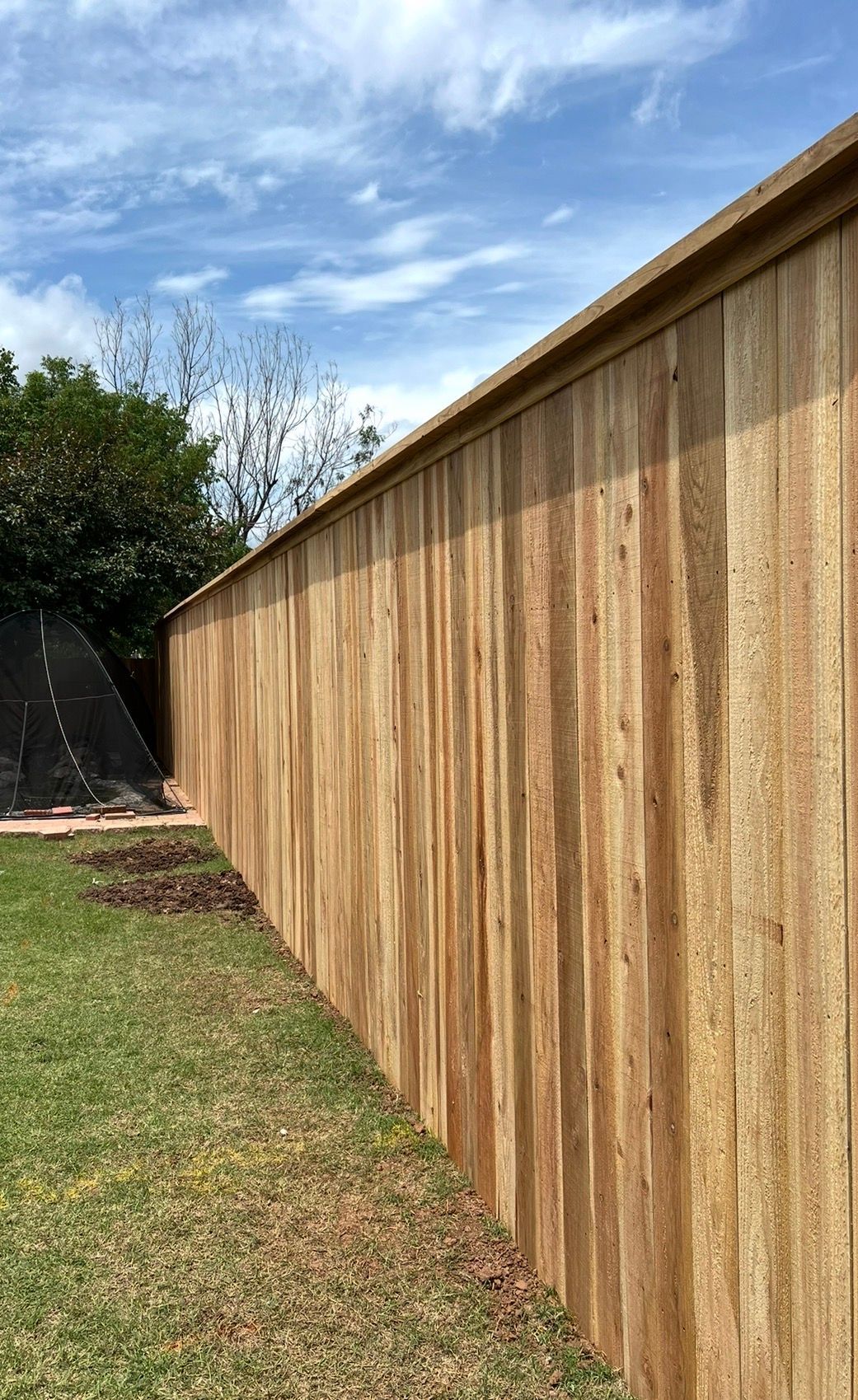 Wooden privacy fence running alongside a grassy yard under a partly cloudy sky
