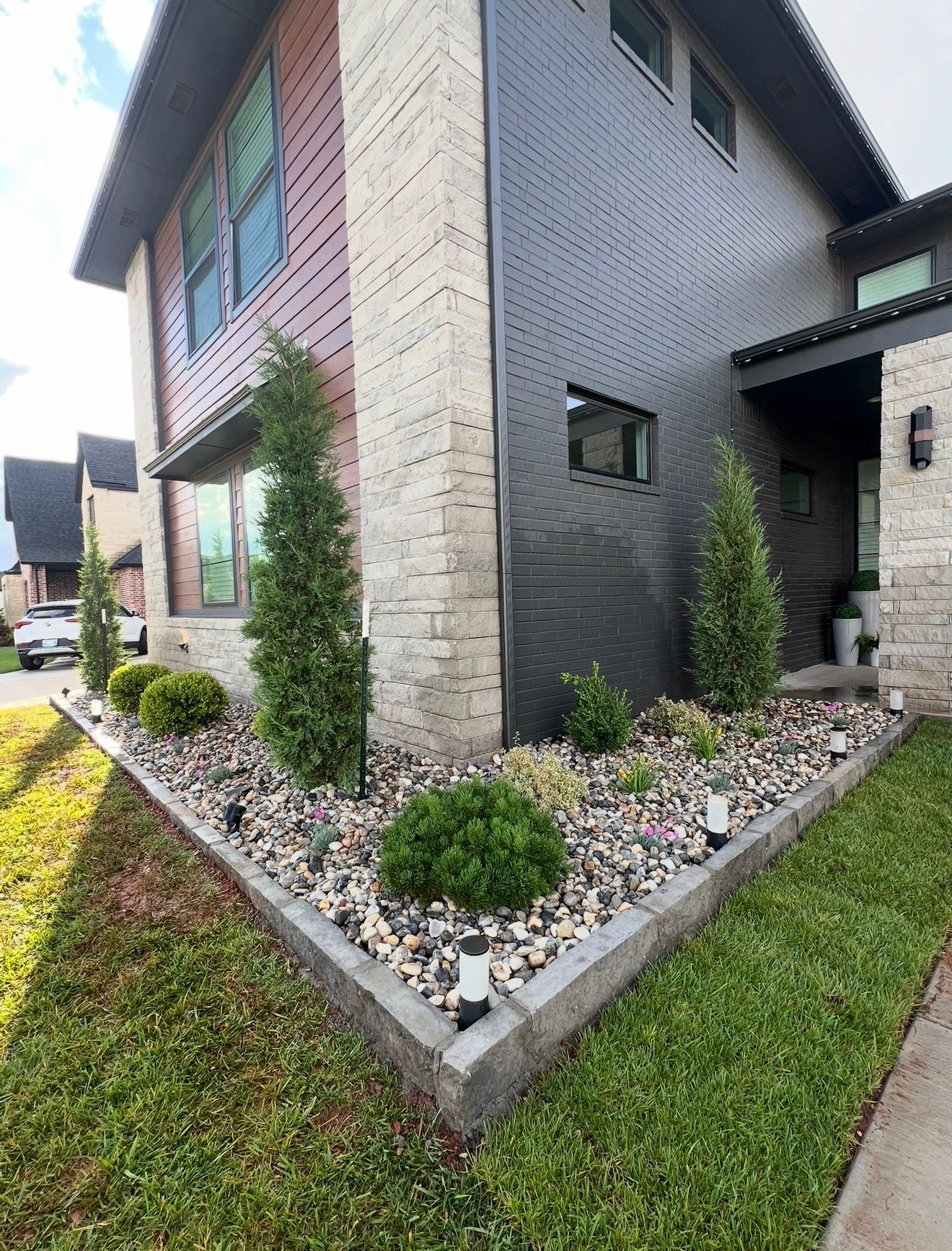 Modern two-story house corner with gray brick exterior and landscaped rock garden along the foundation