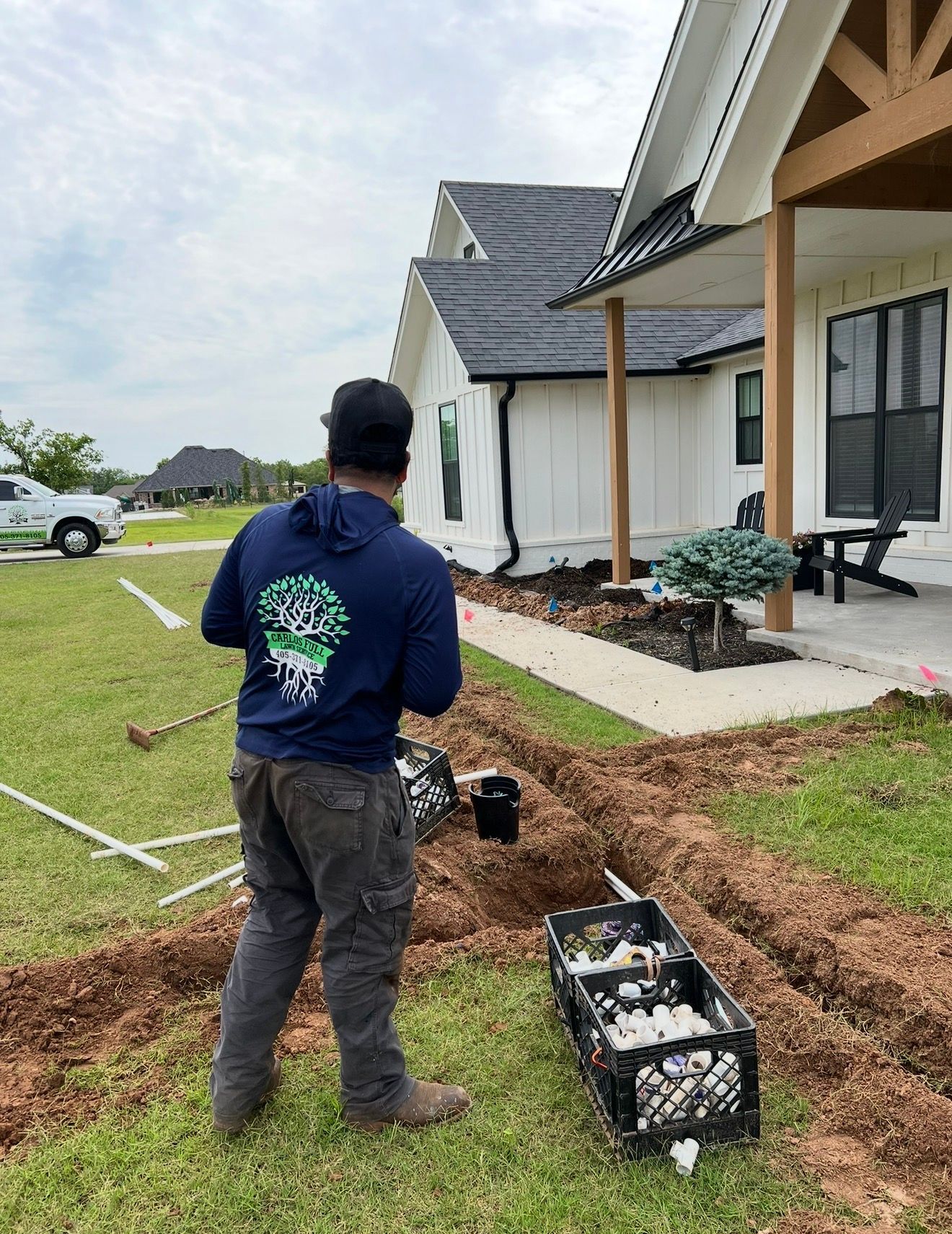 Worker installing irrigation near a house, with trenches and tools in the yard