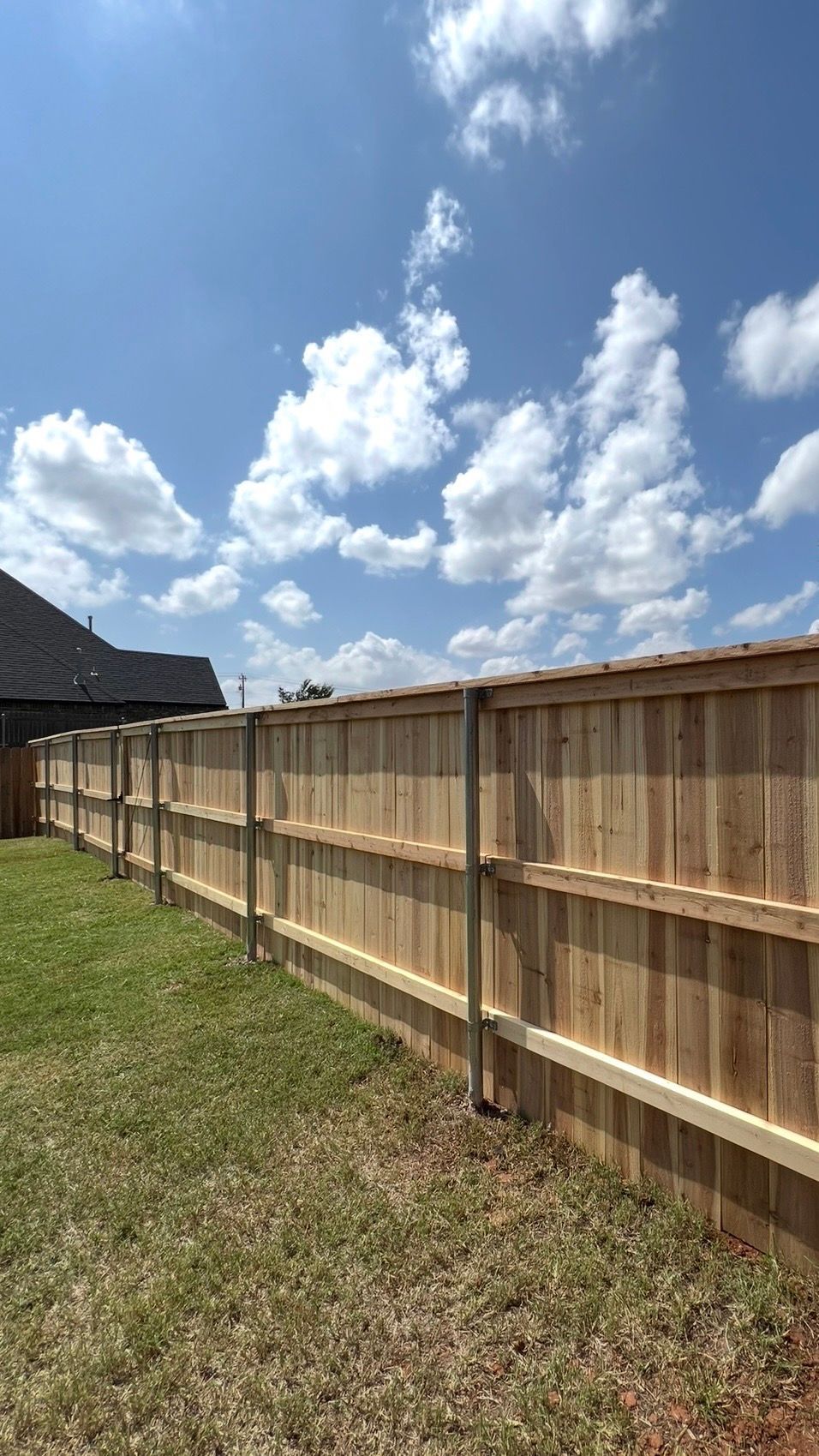 Wooden privacy fence along a grassy backyard under a bright blue sky with clouds