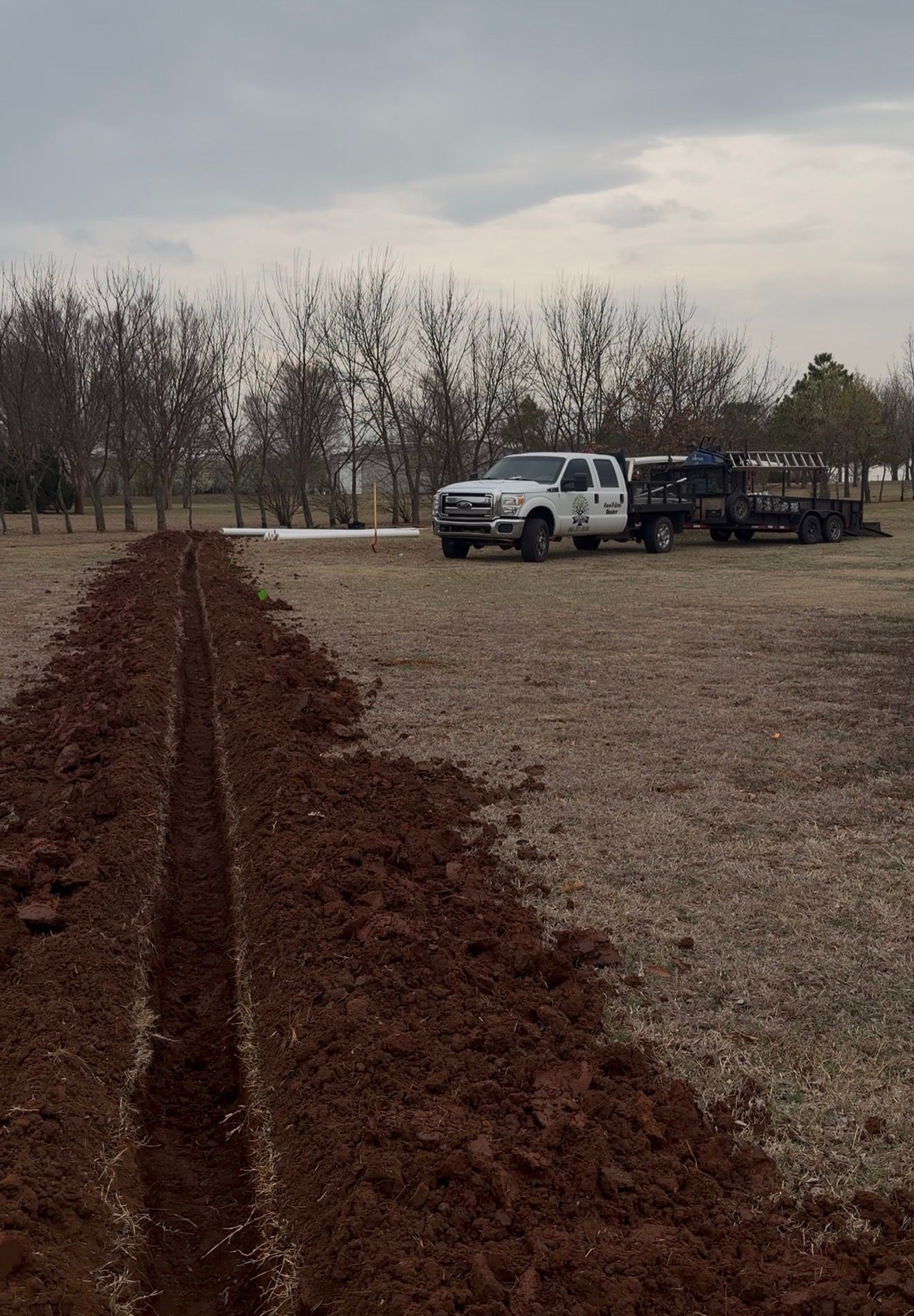Dirt path leading through bare field to white pickup trucks under a cloudy sky