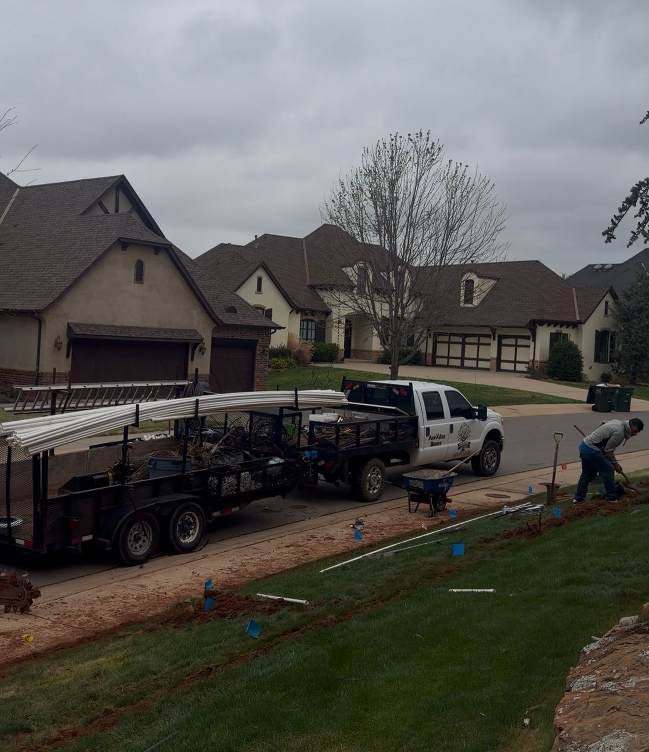Work truck and trailer on a suburban street beside houses, with debris along the curb on a rainy day
