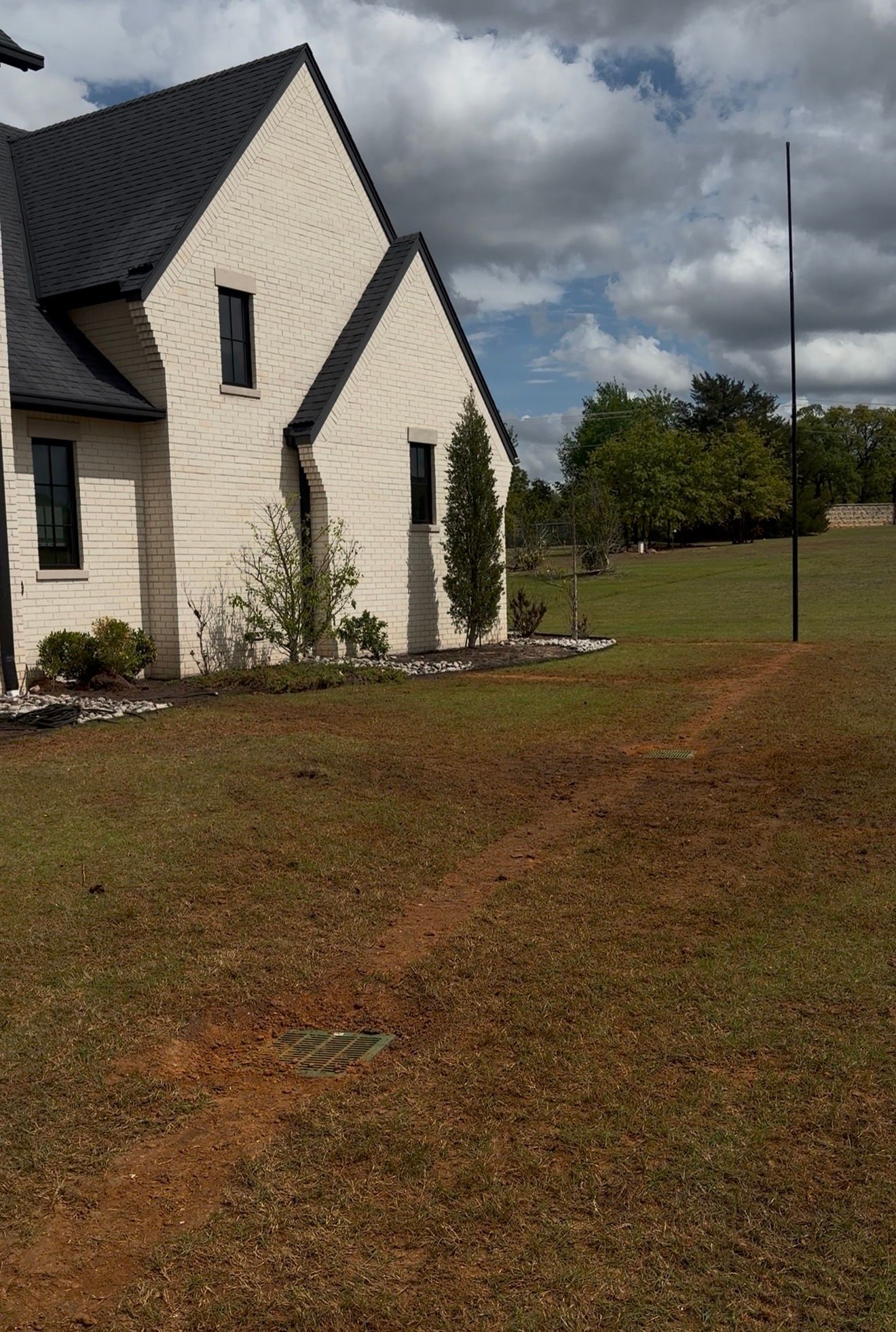 White house with steep black roof beside a grassy yard under cloudy skies
