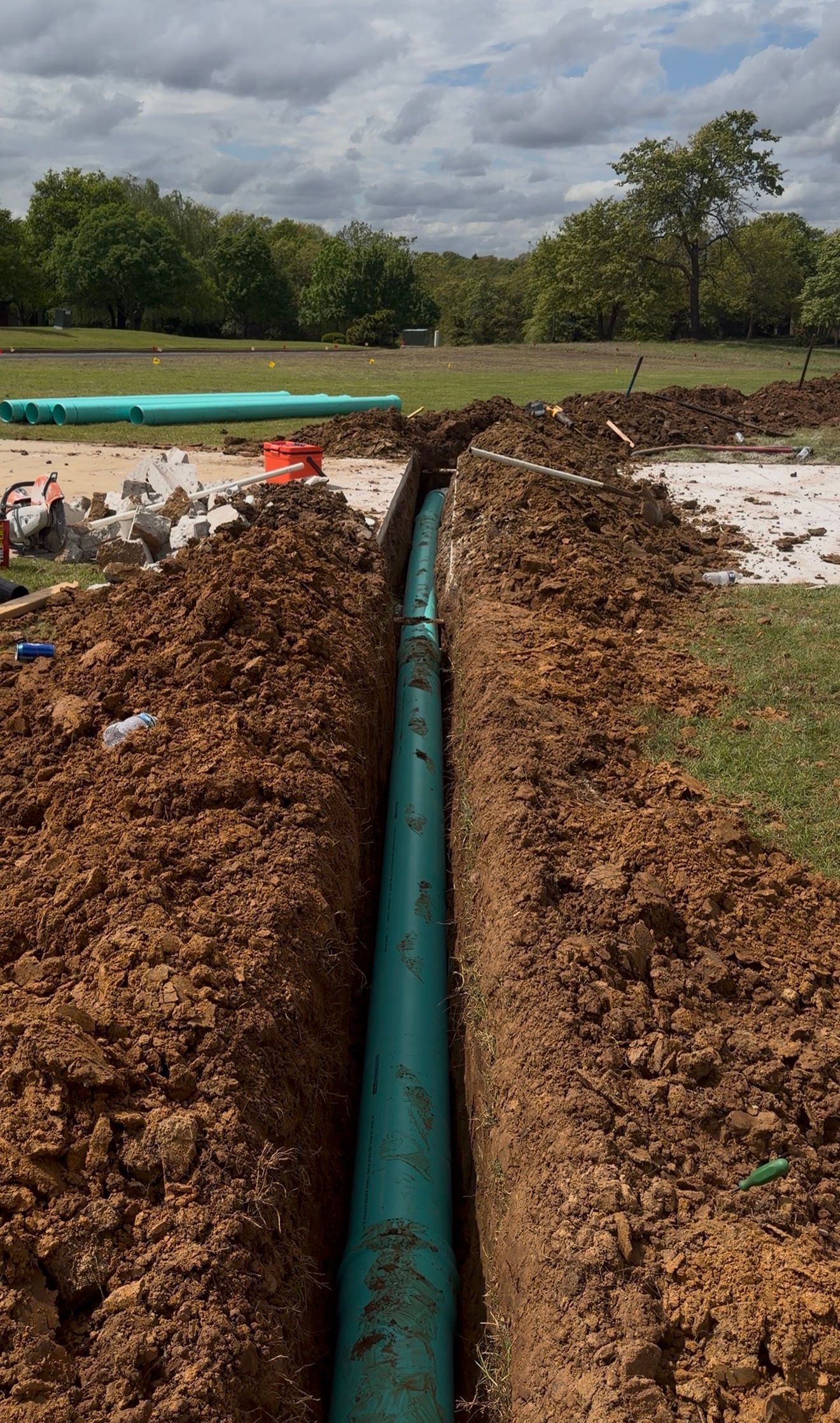 Green pipeline laid in a muddy trench beside an open field under cloudy skies