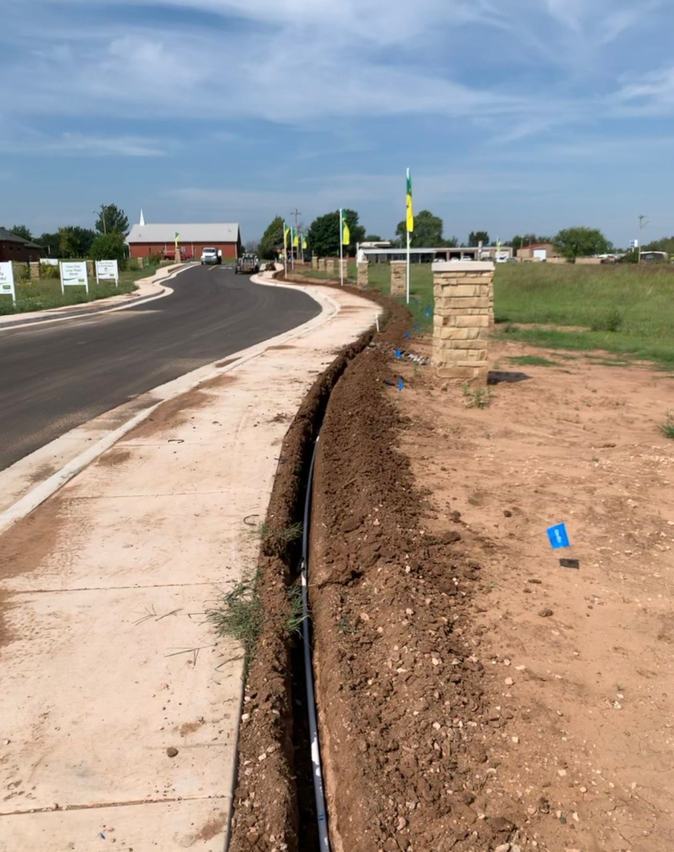 New paved road with open drainage ditch beside a rural roadside under a blue sky