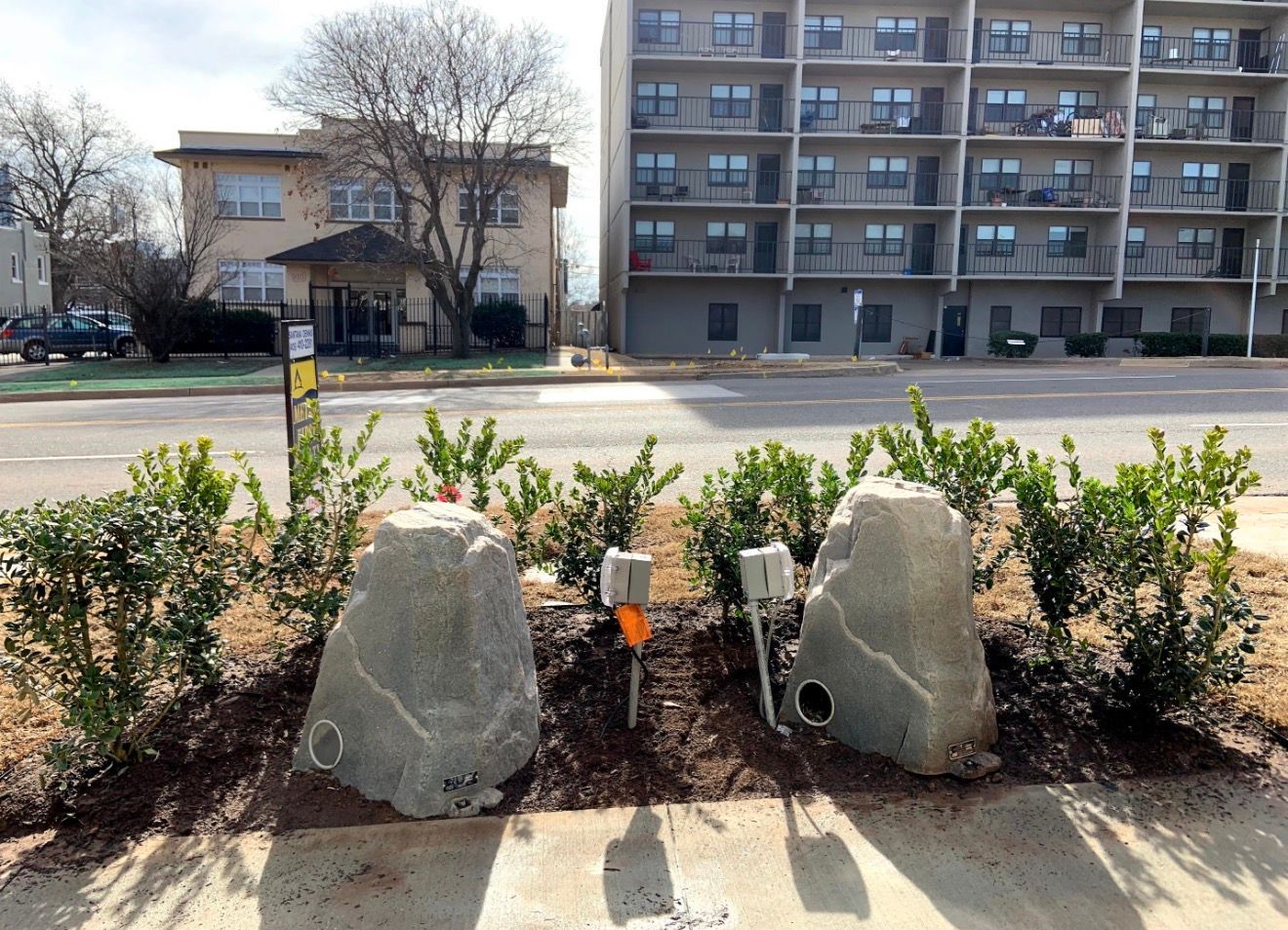 Landscaped street median with rocks and shrubs in front of apartment buildings