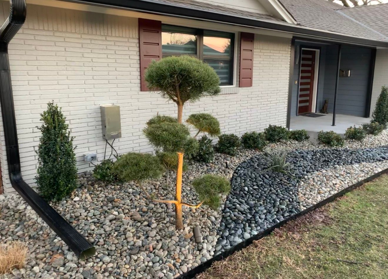 Landscaped front yard with shrubs, a small tree, and gray rock mulch beside a house