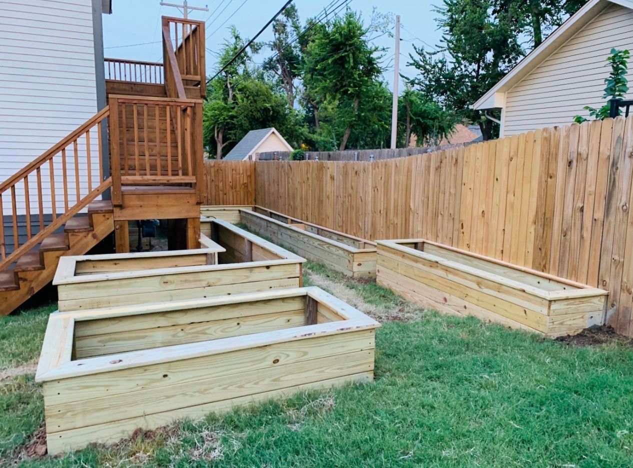 Backyard with wooden deck stairs and framed raised garden beds along a fenced lawn
