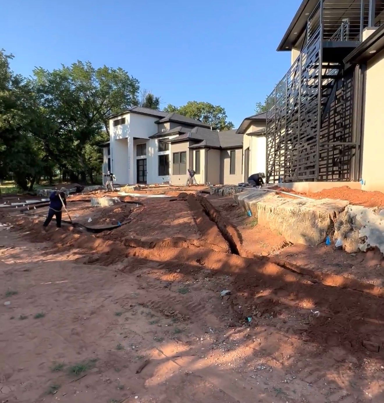 Construction site with red dirt, a worker, and partially built houses under a clear blue sky