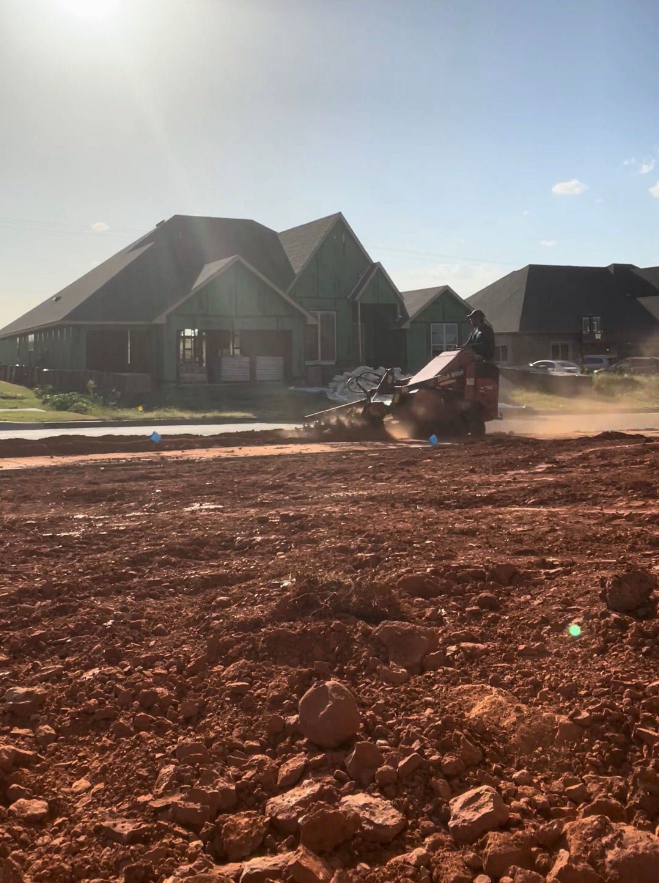 Bulldozer grading a dirt lot in front of new suburban houses at sunrise
