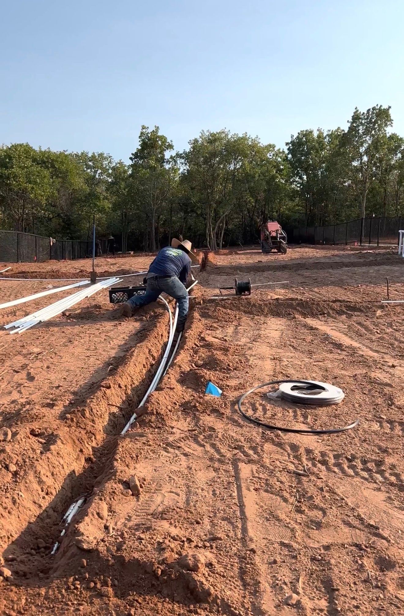 Worker laying long pipes in a muddy construction trench under a clear sky