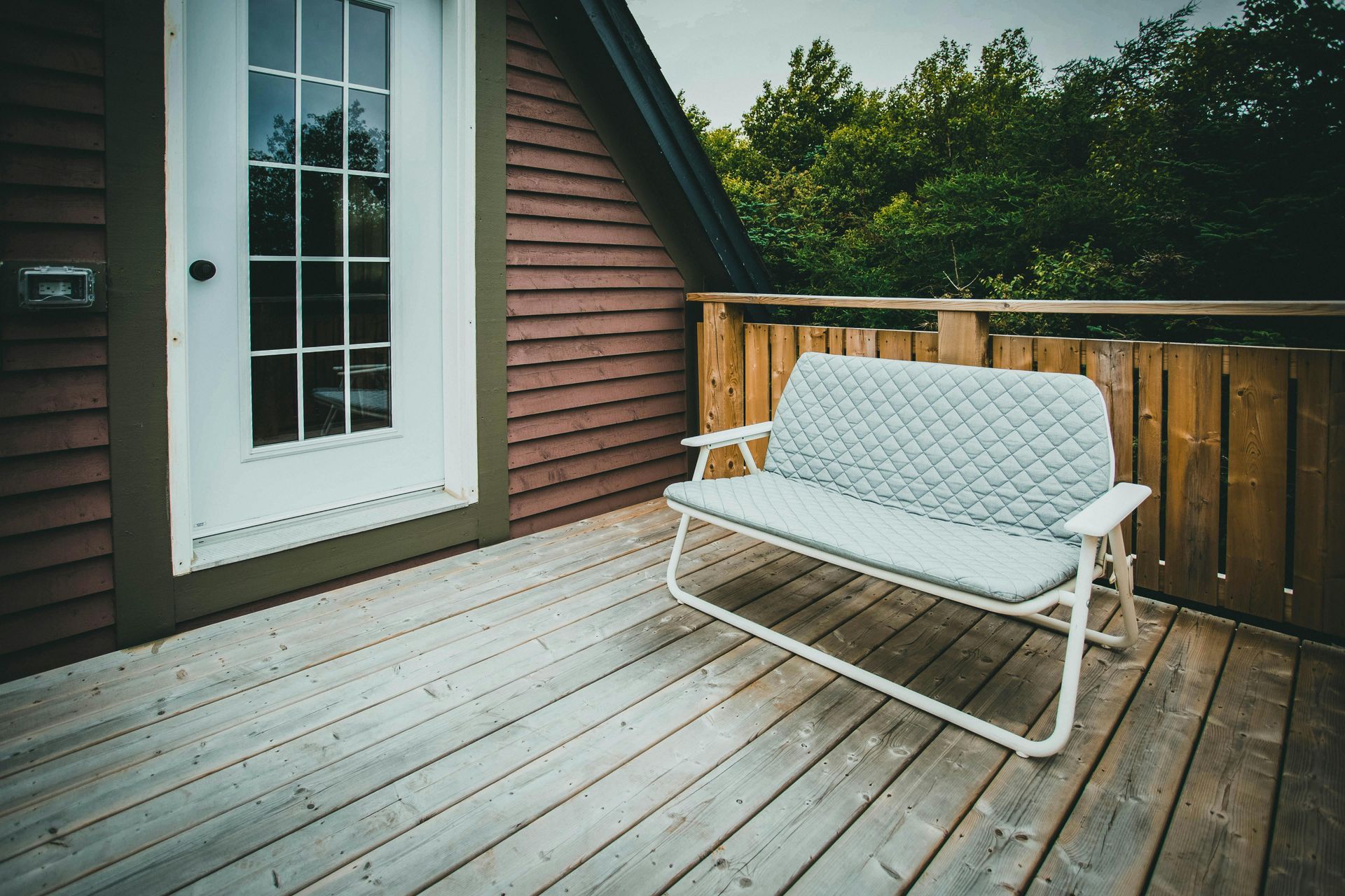 Wooden deck with a white cushioned bench beside a house and railing
