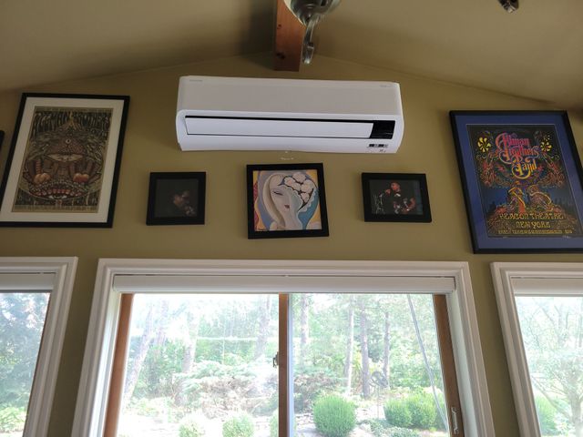 Wall with five framed artworks around a white wall-mounted air conditioner above bright windows