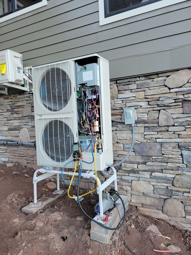 Outdoor HVAC unit on a stand, with exposed wiring and panels, beside a stone house wall