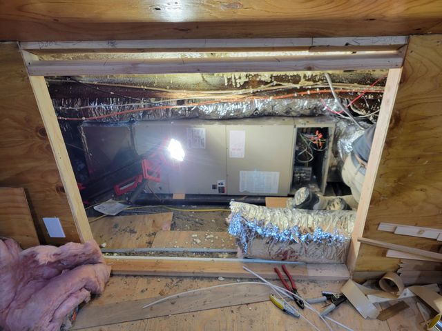 Attic crawlspace with exposed wiring, insulation, and a bright work light over stored equipment