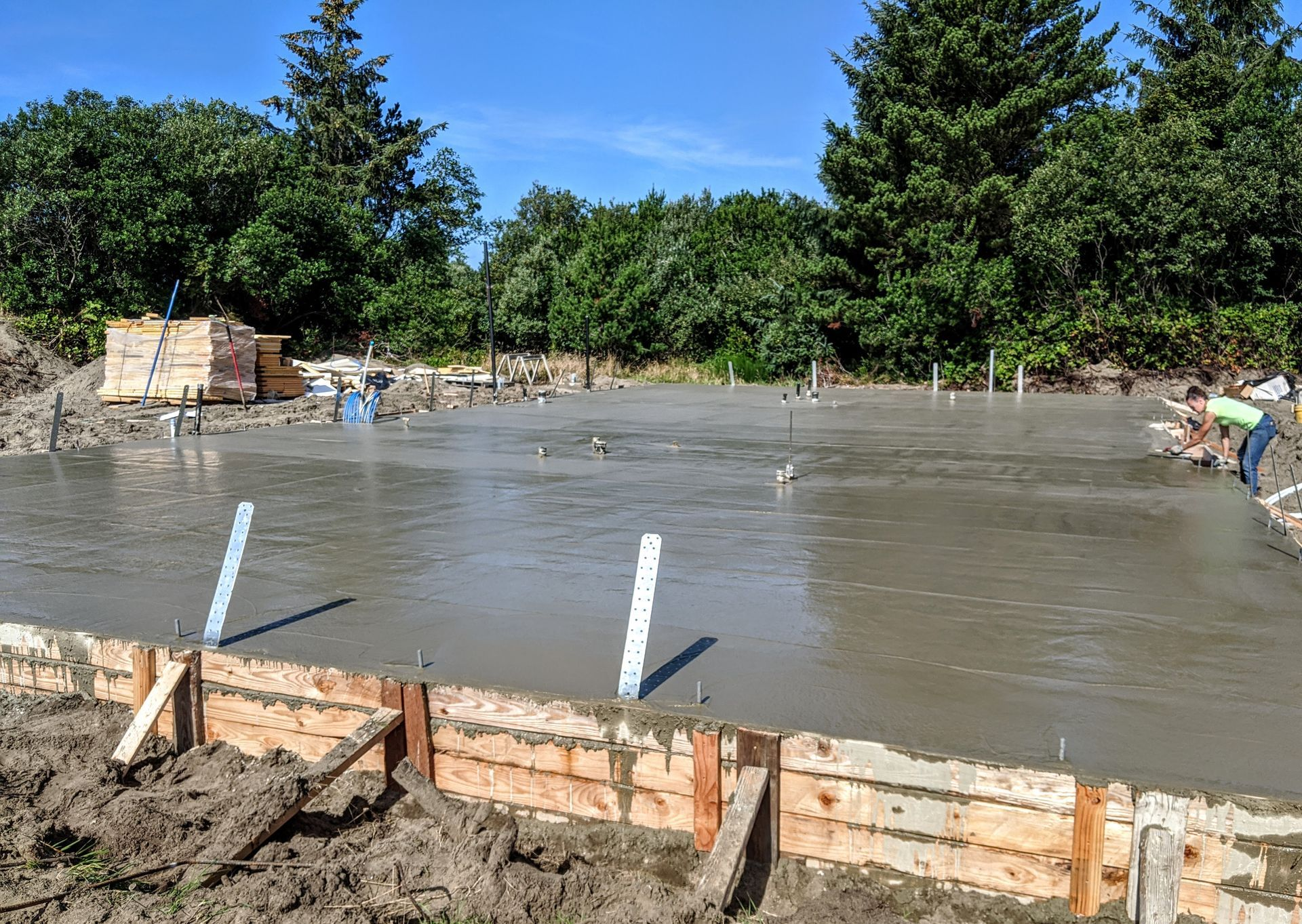 A concrete foundation is being poured in a yard with trees in the background.