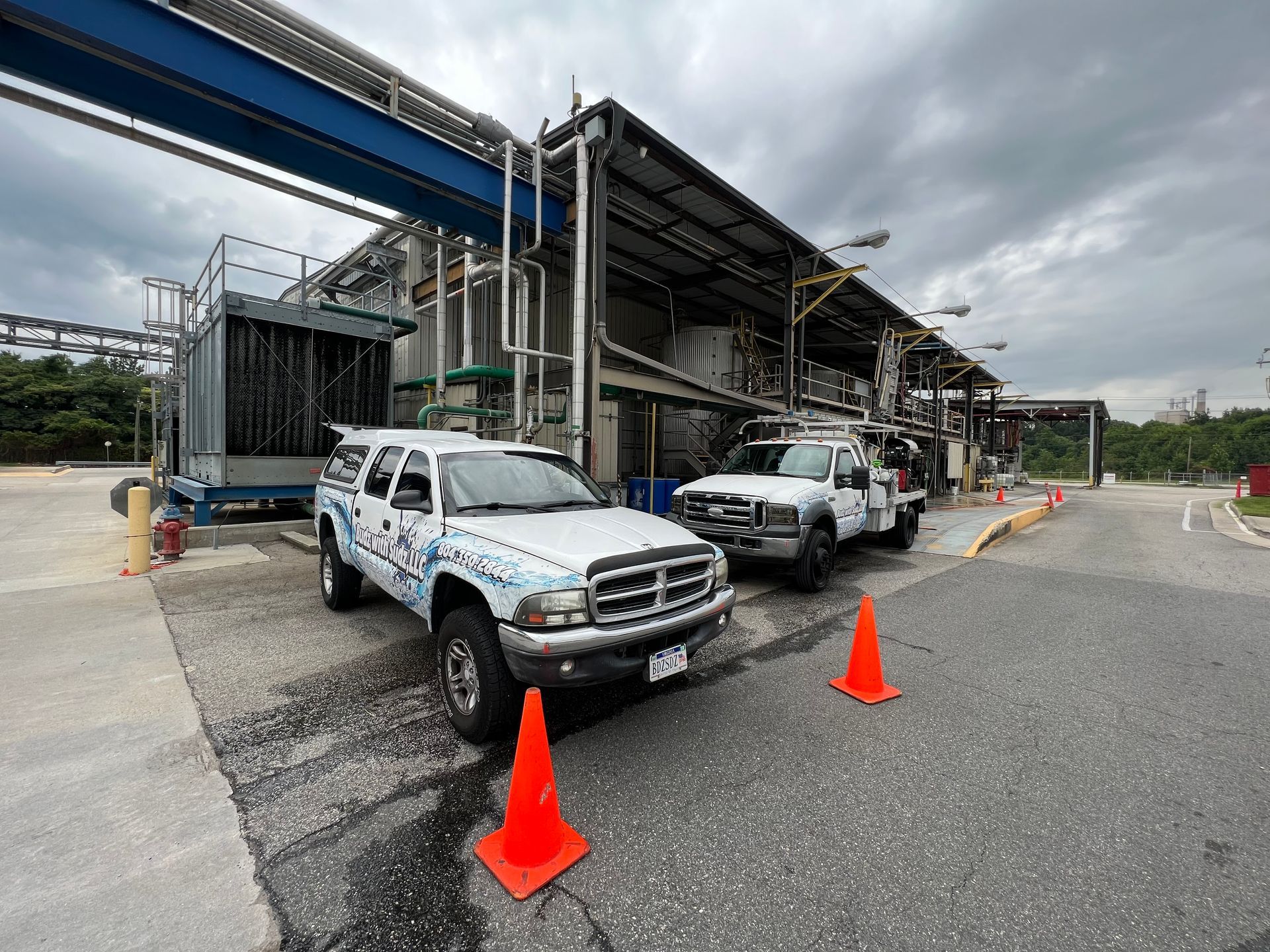 Two white trucks are parked in front of a building with orange cones.