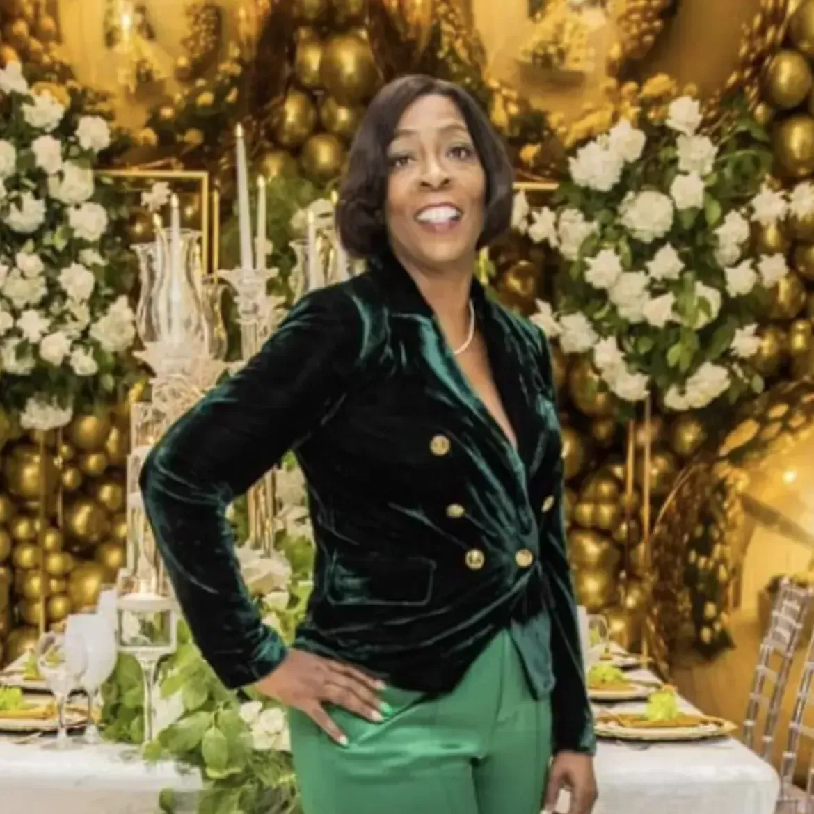 A woman in a green jacket and green pants is standing in front of a table.