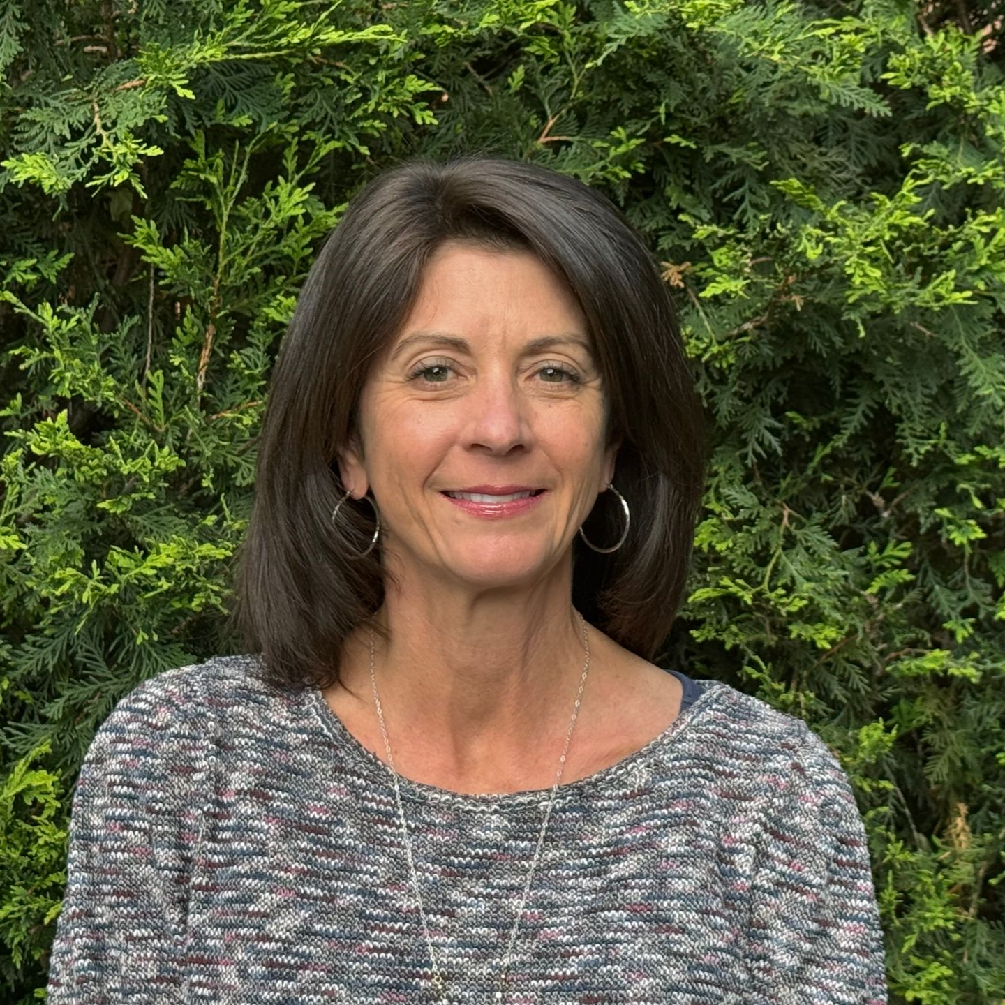 A woman in a black shirt is smiling in front of a tree.