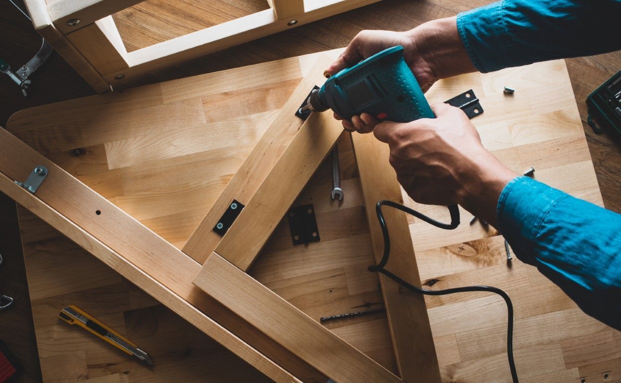Hands using a drill to assemble a wooden frame on a workbench