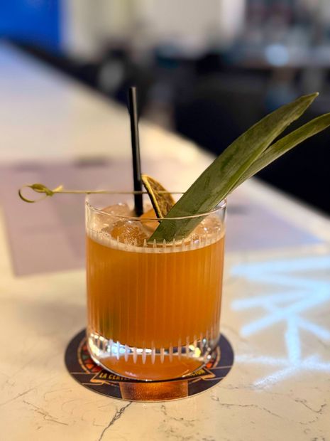 Orange cocktail with black straw and green leaf garnish on a bar counter