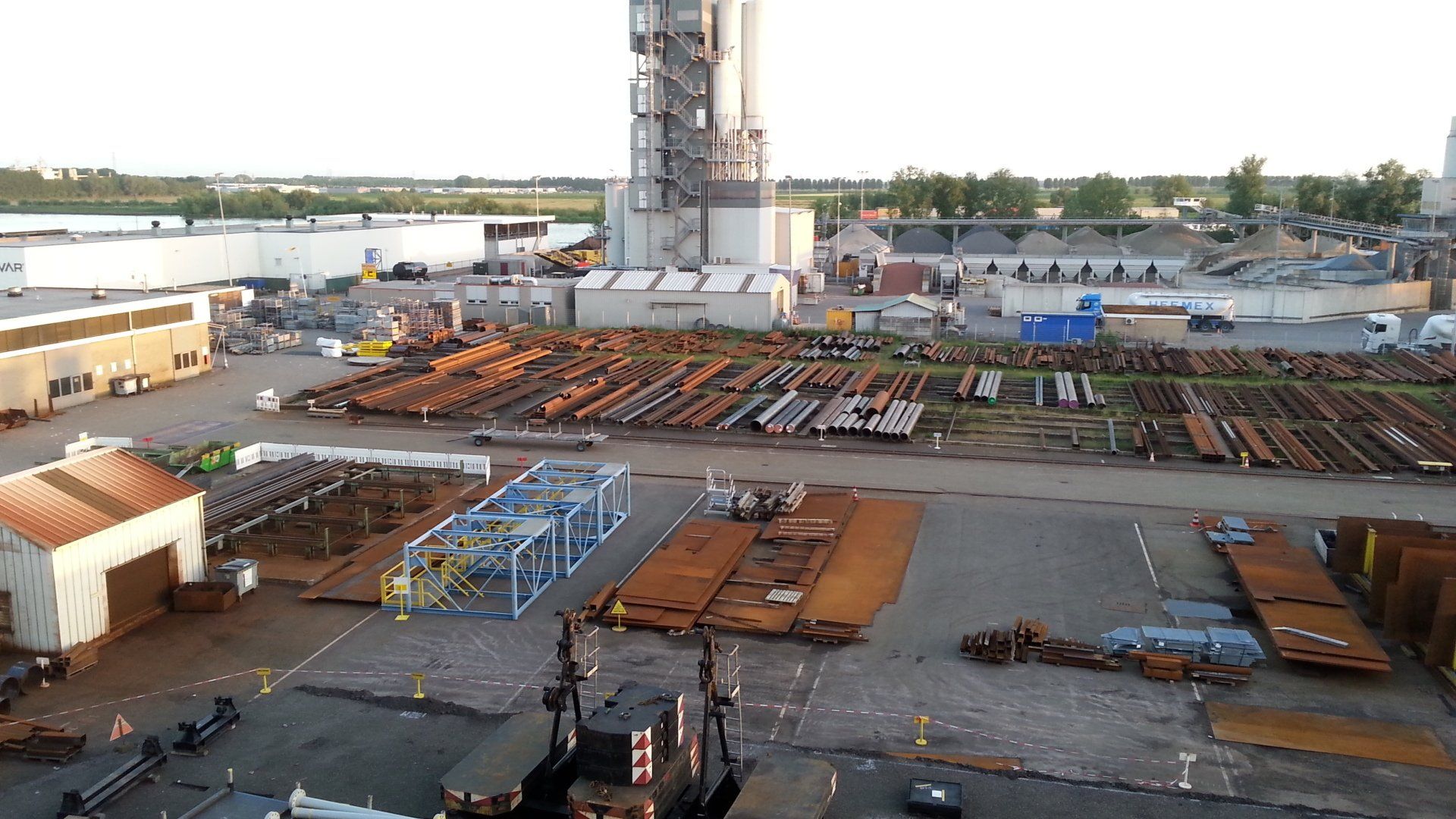 Industrieterrein met stalen balken, tanks en een grote toren.