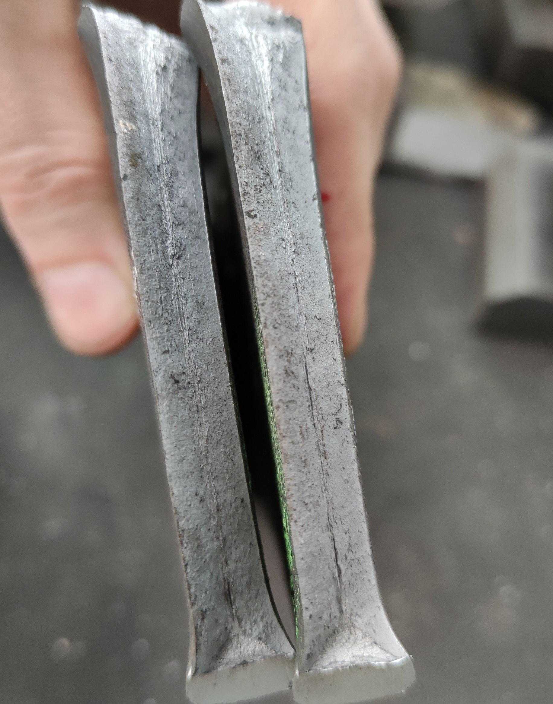 Twee metalen stukken naast elkaar gehouden, die een ruw, gehavend oppervlak laten zien.