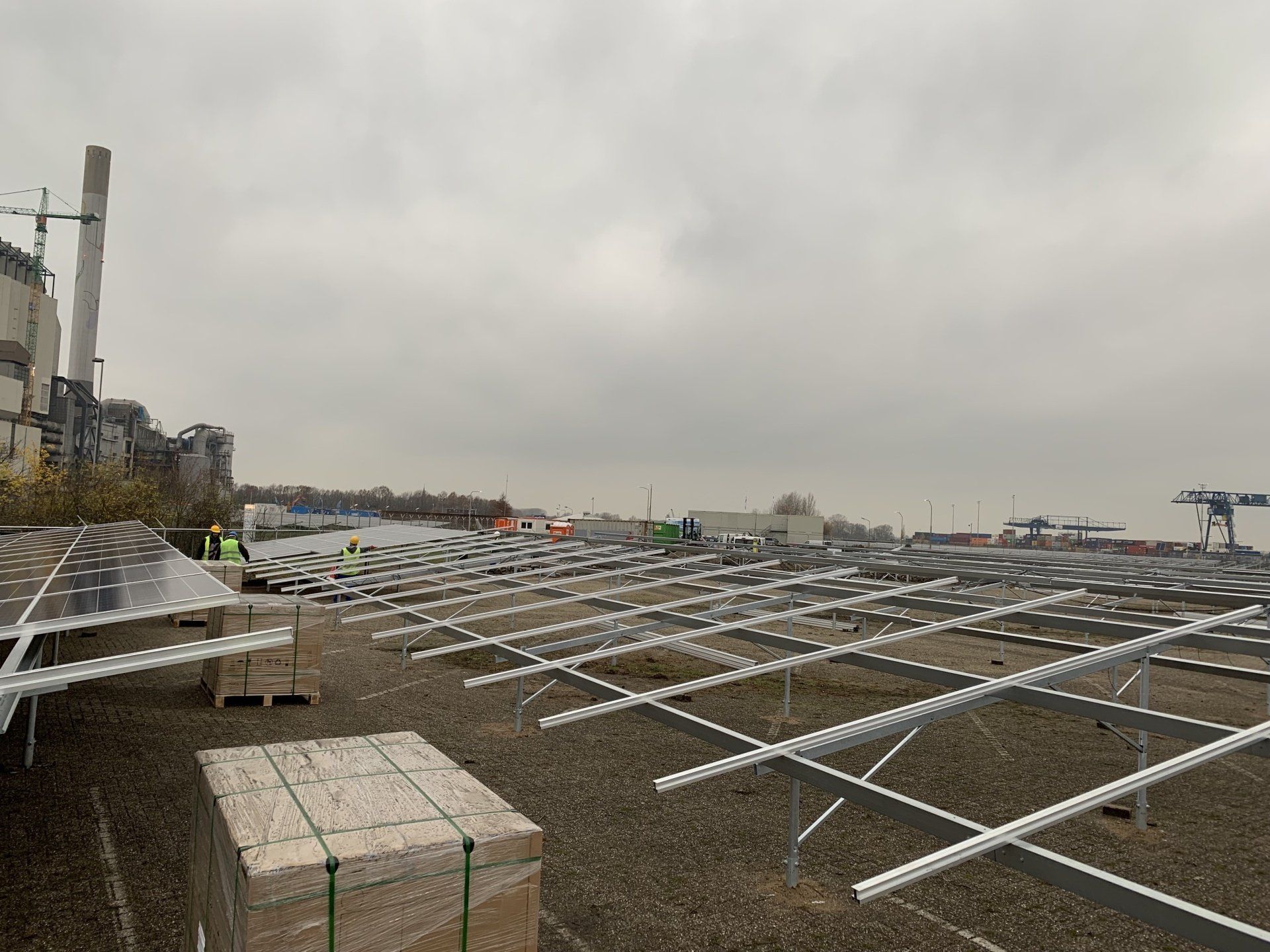Installatie van zonnepanelen op een dak bij bewolkt weer; elektriciteitsnet en gebouw op de achtergrond.
