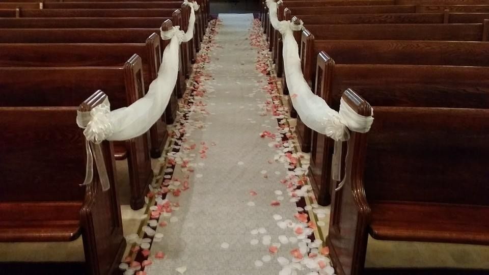 White rose petals lining a church aisle with pews draped in white ribbons