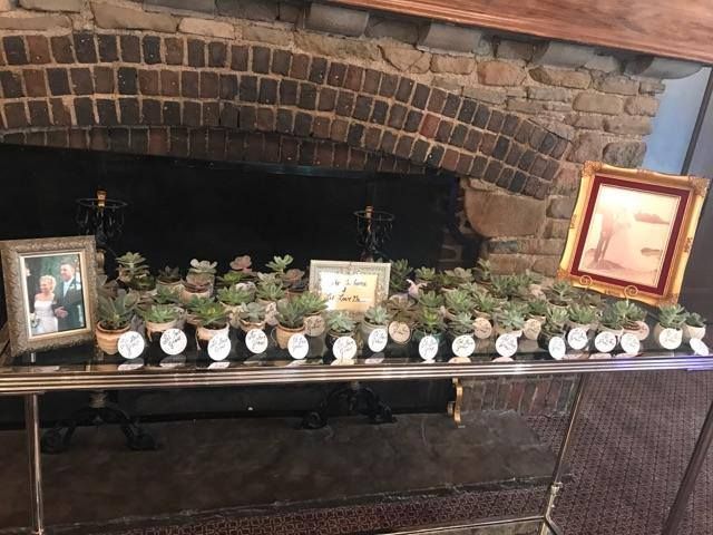 Fireplace mantel with framed photos and a row of small white decorative figurines and plants under a brick arch.