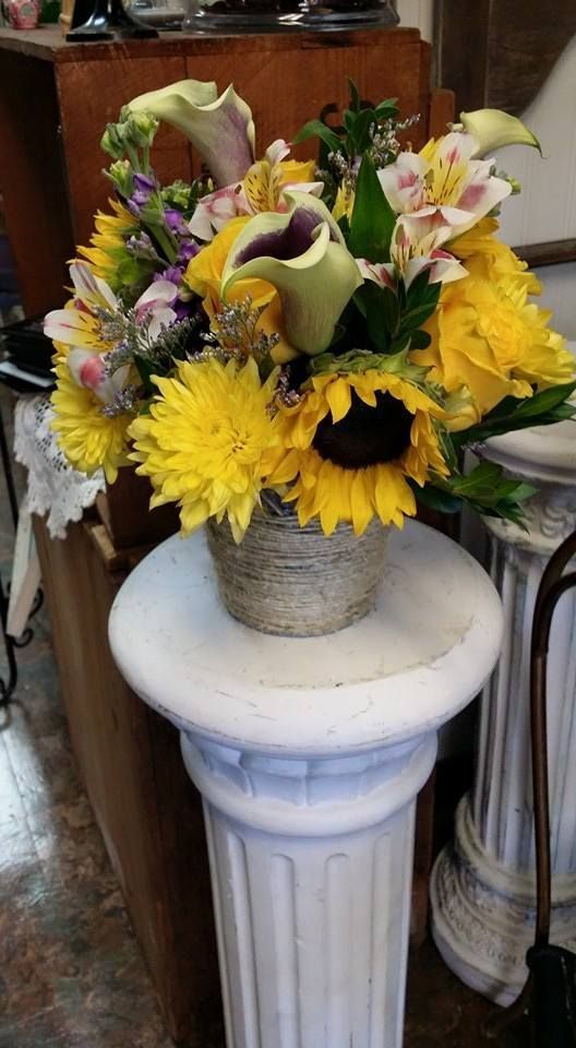 Mixed flower bouquet with yellow sunflowers and lilies in a vase on a white pedestal table