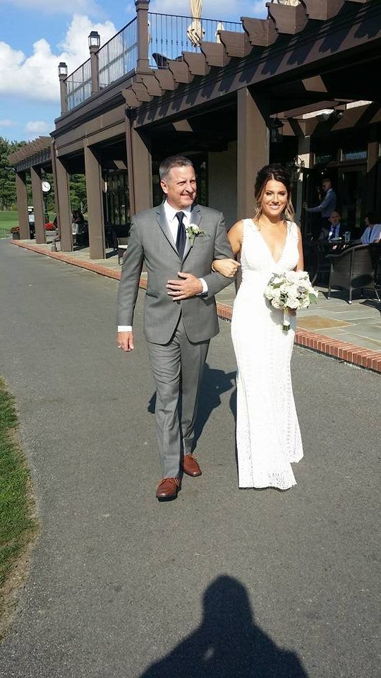 Bride and groom walking outdoors, bride in white dress holding bouquet, groom in gray suit.