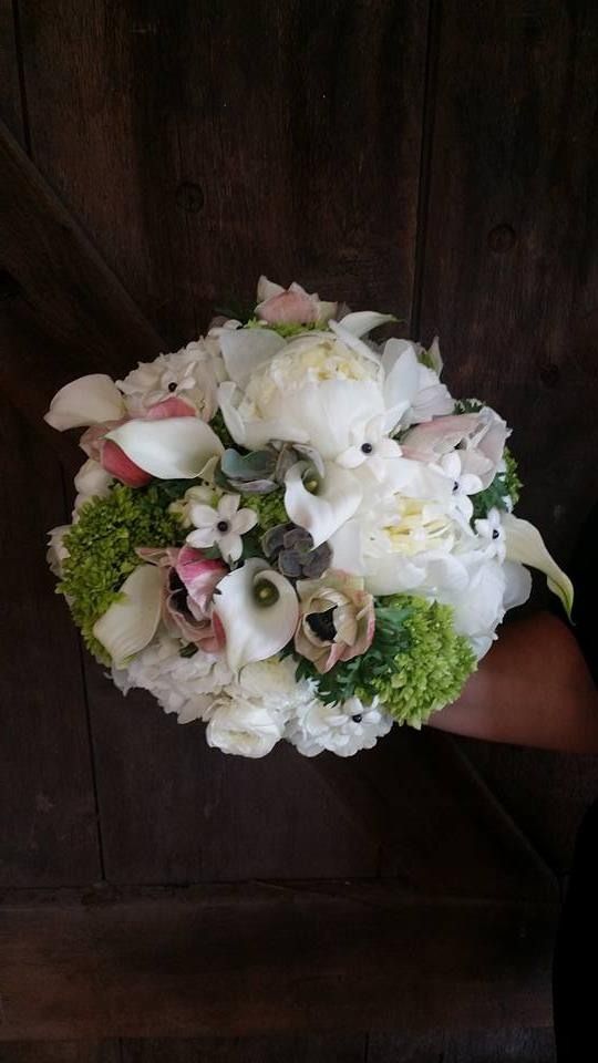 White floral bouquet with green accents held against a dark wooden background