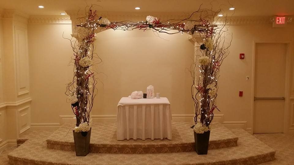 Decorated indoor wedding arch with white table and floral arrangements on a carpeted stage