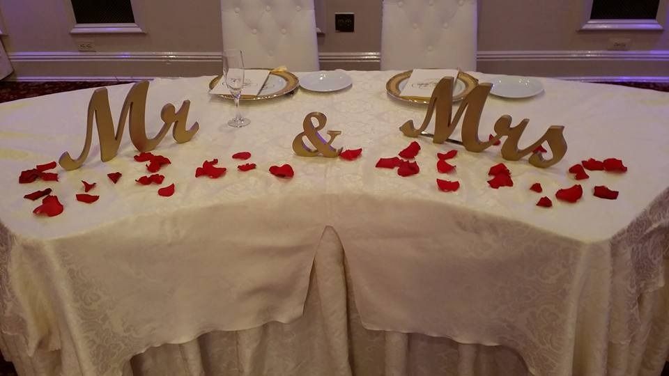 Gold “Mr & Mrs” sign on a table with red rose petals at a wedding reception