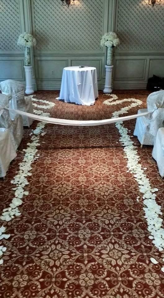 Decorated indoor aisle with red carpet, white draped chairs, and a small table at the end