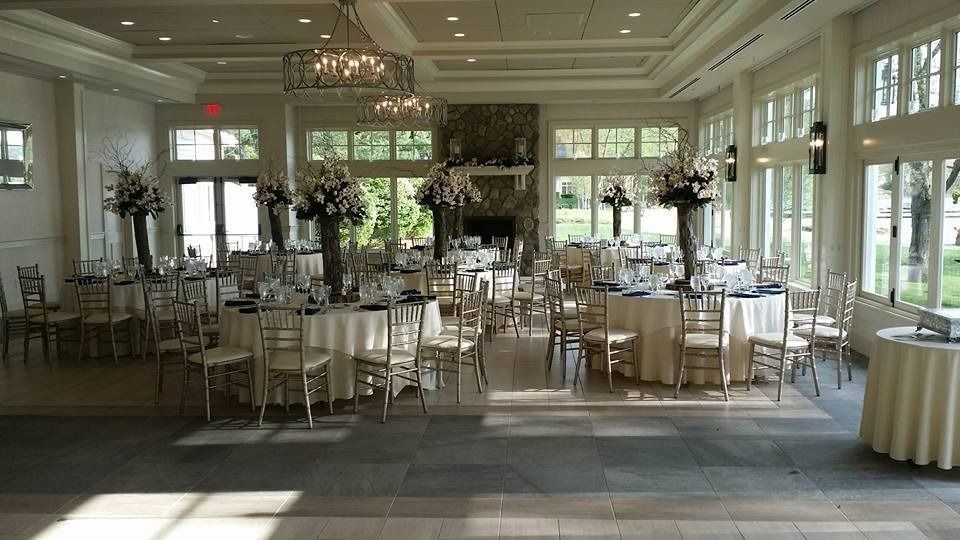 Elegant reception hall with round tables, white chairs, and large windows letting in daylight