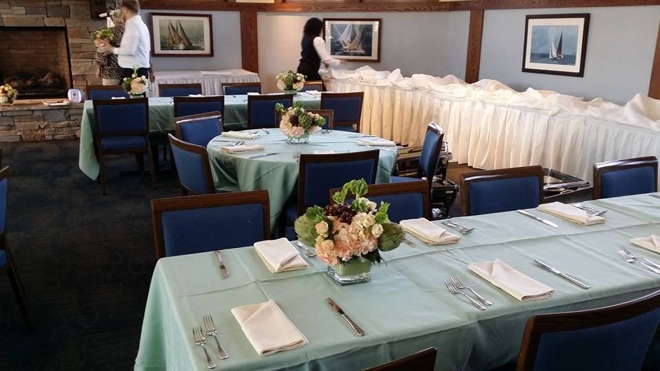 Formal dining room with teal table settings, white chair covers, and framed wall art; two people arrange tables.