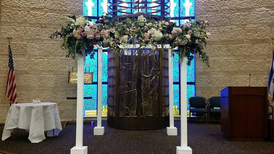 Wedding canopy with white posts, flowers, and stained-glass backdrop in a church sanctuary