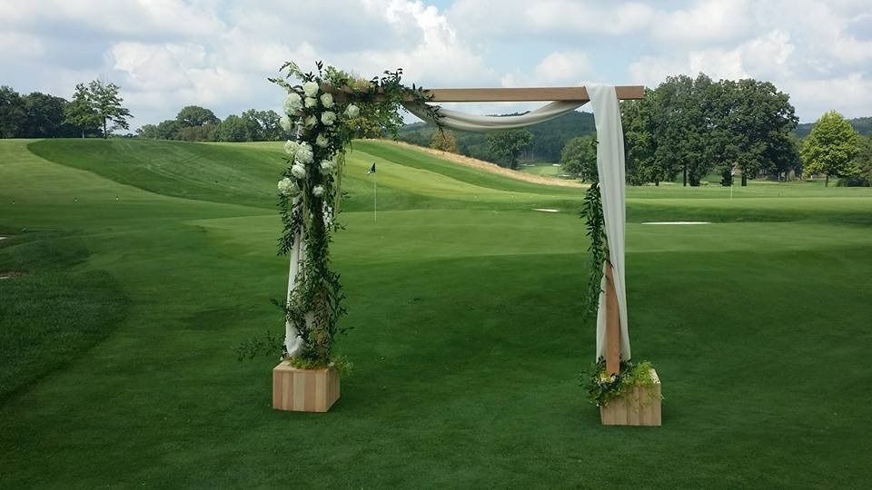 Flower-decorated wedding arch on a green golf course with hills and trees in the background