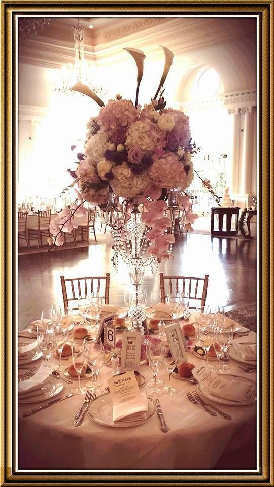 Elegant banquet table with tall floral centerpiece and gold place settings in a sunlit ballroom
