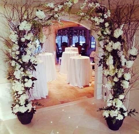 Flower-covered archway framing a wedding reception area with round tables and white tablecloths