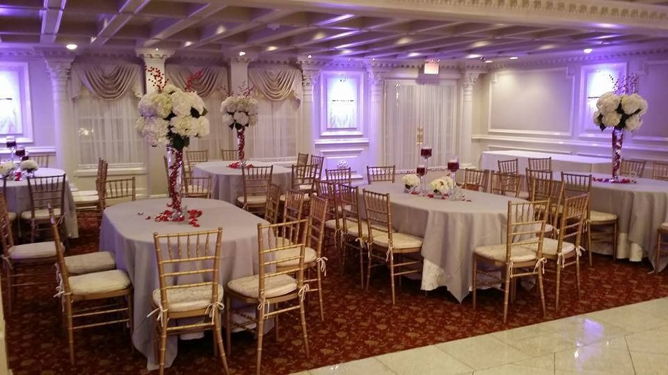 Elegant banquet hall with round tables, gold chairs, white linens, and floral centerpieces under purple lighting