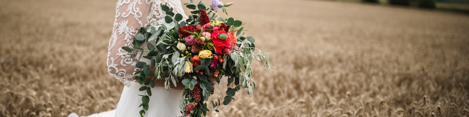 Person in a white dress holding a bouquet of red and white flowers in a dry field